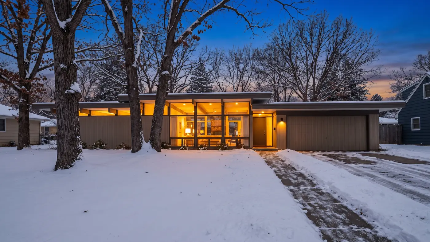 A mid-century modern home with wide windows on a snowy evening in Edina